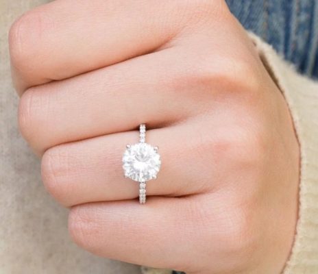 A woman's hand showing a single band, 4 prong diamond engagement ring.