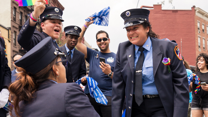 A woman proposing to her partner surrounded by people during an FDNY medic pride parade