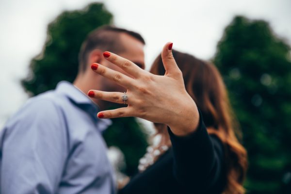 A couple kissing with the woman's hand wearing an engagement ring that covers their faces