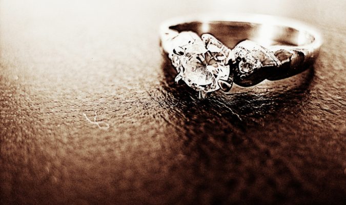 Engraving engagement ring designed with round-shaped diamond ring placed in a sandy- textured surface