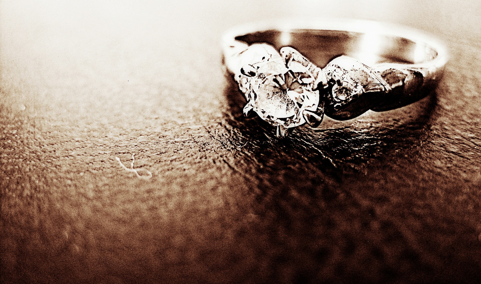 Engraving engagement ring designed with round-shaped diamond ring placed in a sandy- textured surface