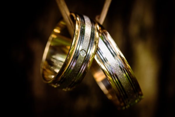 Focus view of couple gold wedding bands in a bezel men's ring setting hang up on a branch