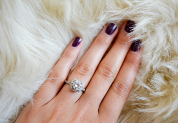 A woman's hand wearing cushion cut halo diamond ring in a furry cloth background