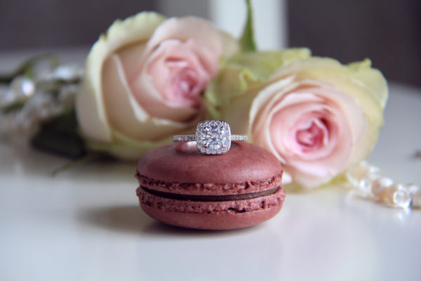 An asscher shape diamond ring on a macaron with pink roses at the background
