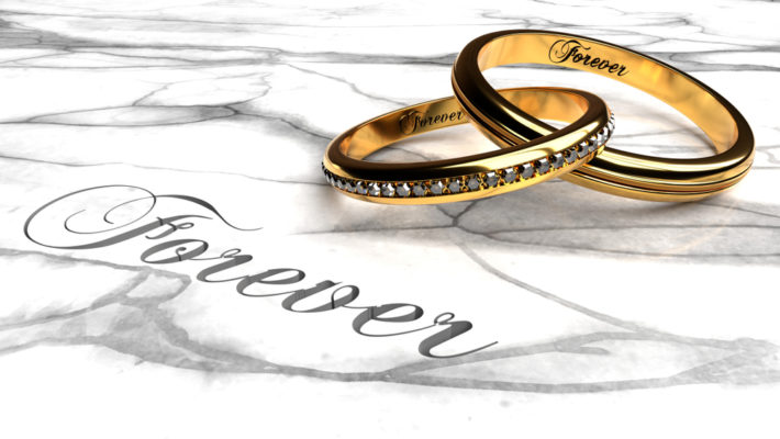 Two gold wedding bands joined together with engraved word 'forever' on a white marble table