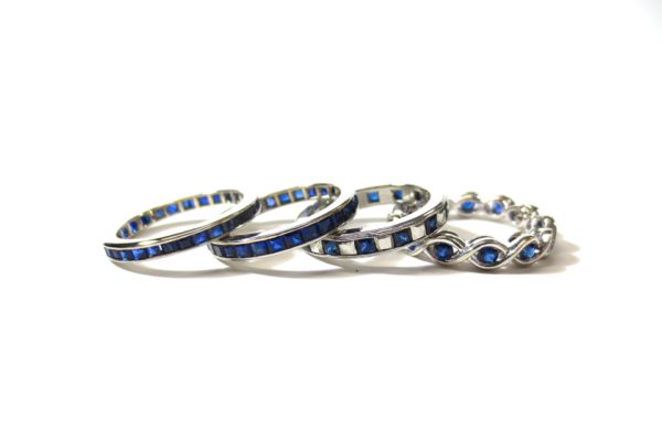 Four rings with sapphire diamonds on its band laying on top of another in a white space