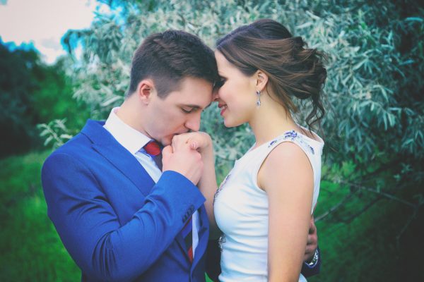 man wearing blue coat kissing her woman's hands with a custom engagement ring