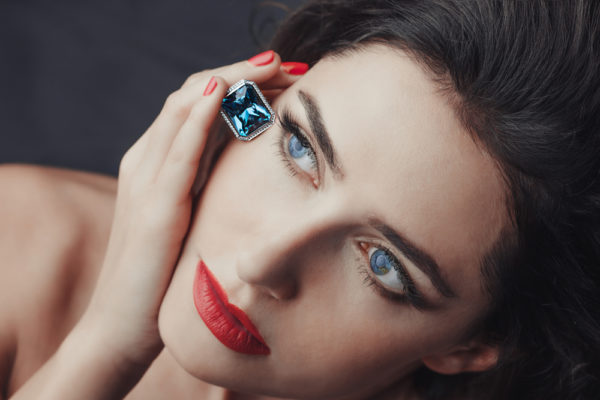 A face of a woman placing a blue radiant-cut sapphire engagement ring on her right cheek