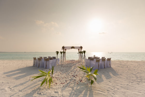 A setup of a beach wedding, alongside the aisle are chairs covered in white cloth perfect wedding destinations