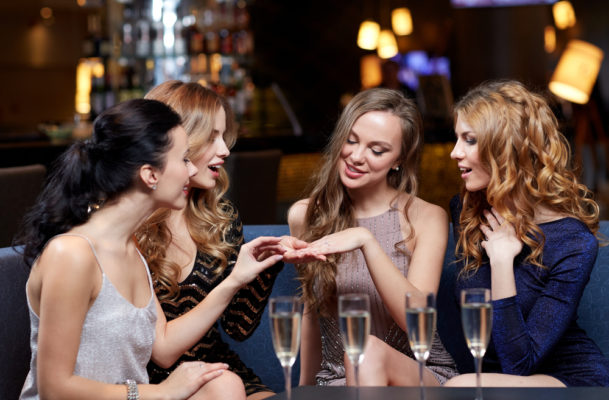 A group of ladies looking at their friend's engagement ring with coloured diamonds