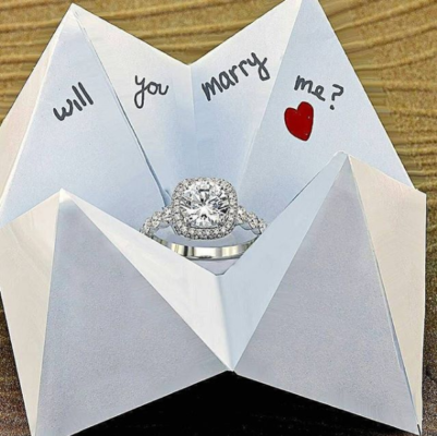Paper fortune teller with a ring in round cut halo engagement ring setting